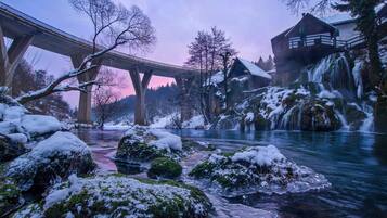 A winter scene with a bridge, a cabin, and a flowing river.