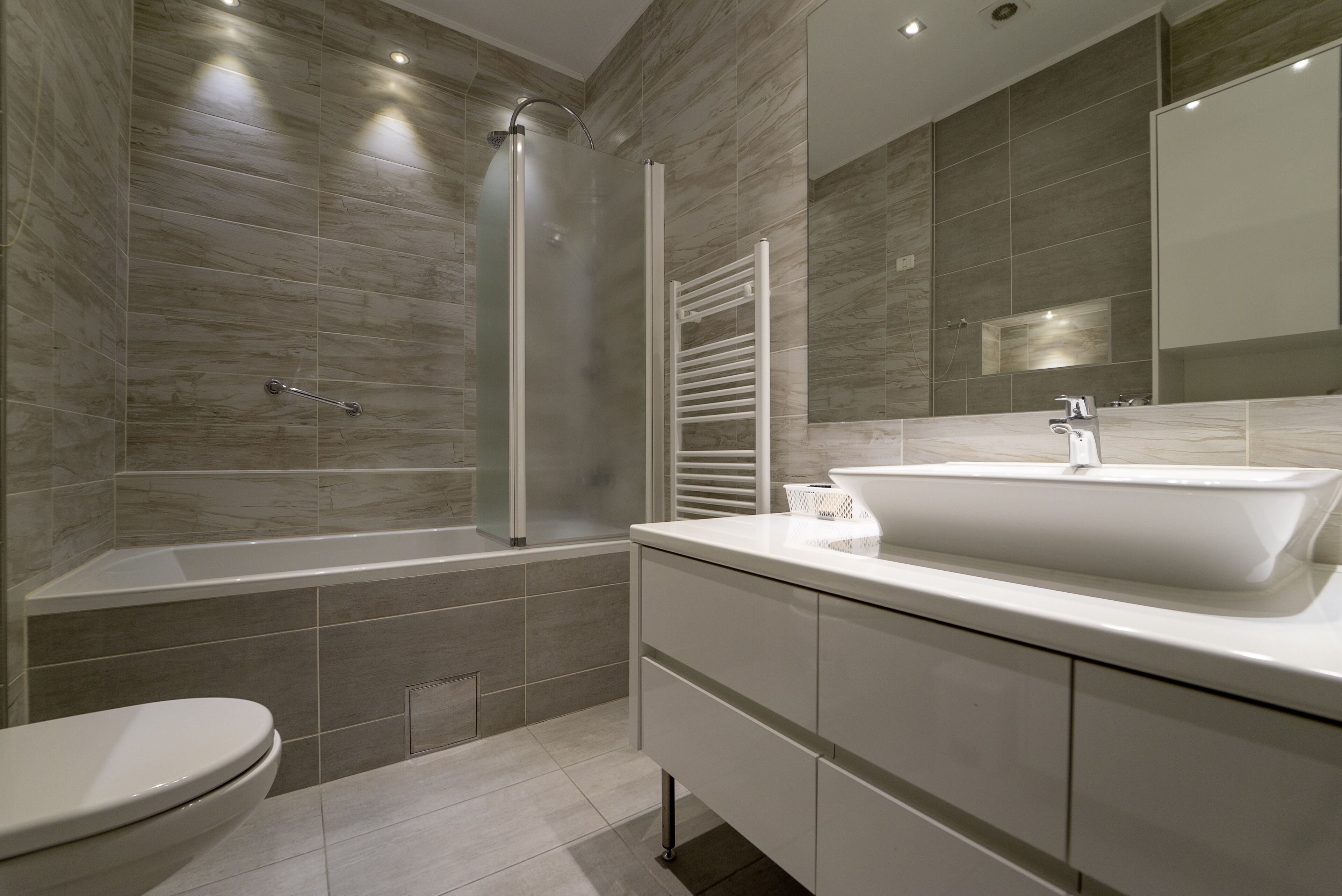 Un baño moderno con ducha de mampara de vidrio, lavabo blanco y un espejo grande.