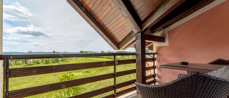 Un balcón con vistas a un paisaje verde, una silla de mimbre y una mesa.