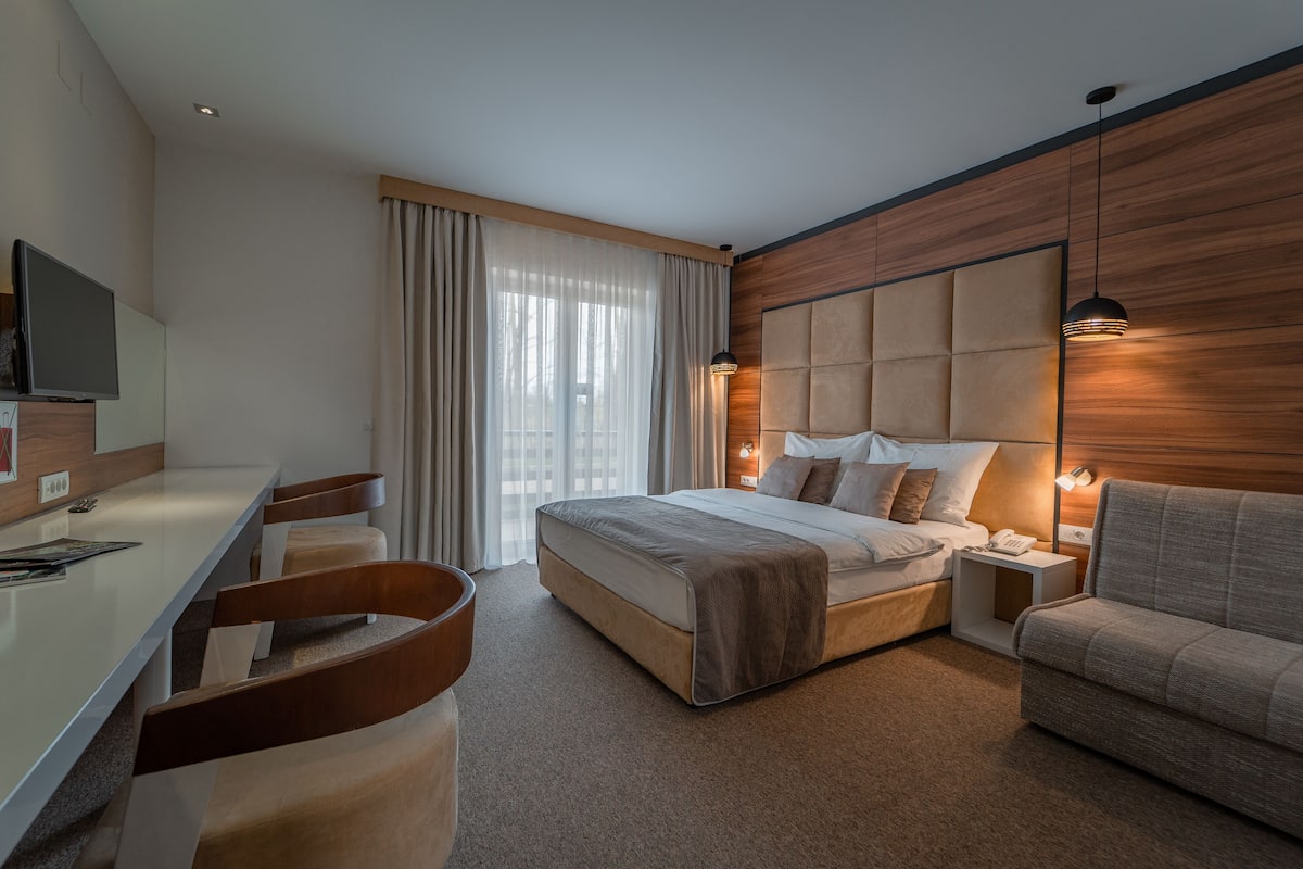 A modern hotel room with a large bed, a sofa, a desk, and a TV.