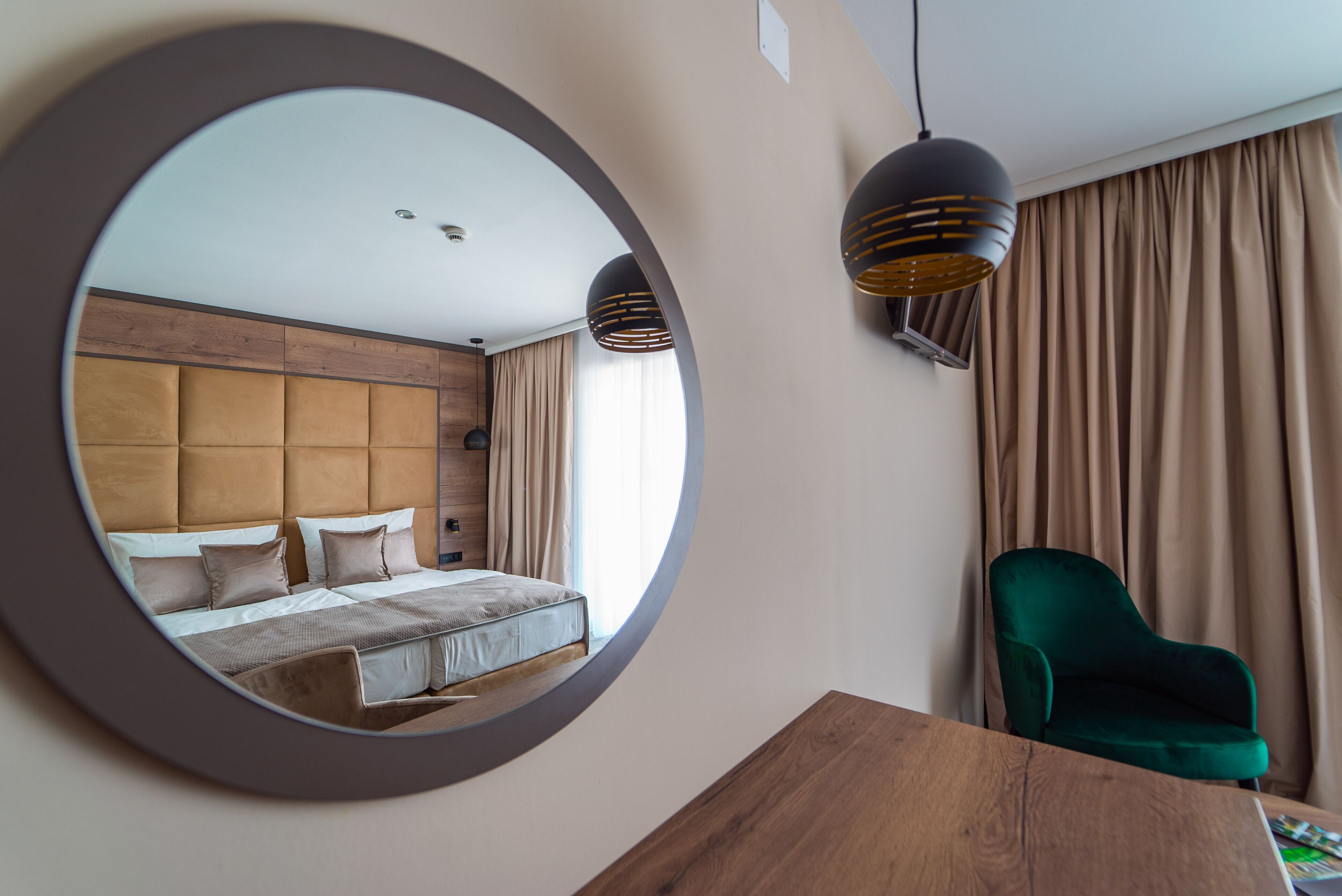 Een hotelkamer met een grote spiegel, een houten hoofdbord, een groene fauteuil en een houten tafeltje.