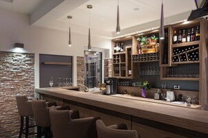 Un área de bar moderna con una pared de piedra, estantes de madera con botellas de vino y taburetes de bar.