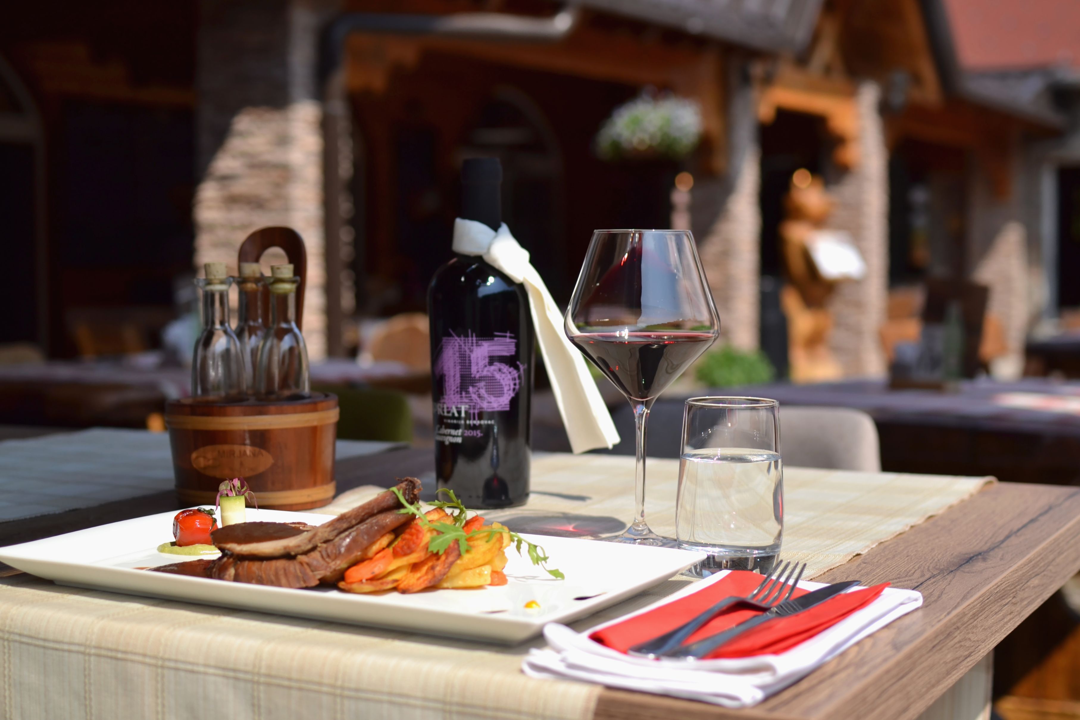 Una mesa de comedor preparada con una botella de vino, una copa de vino tinto, un vaso de agua, un plato de comida y un cofre de madera para vino.