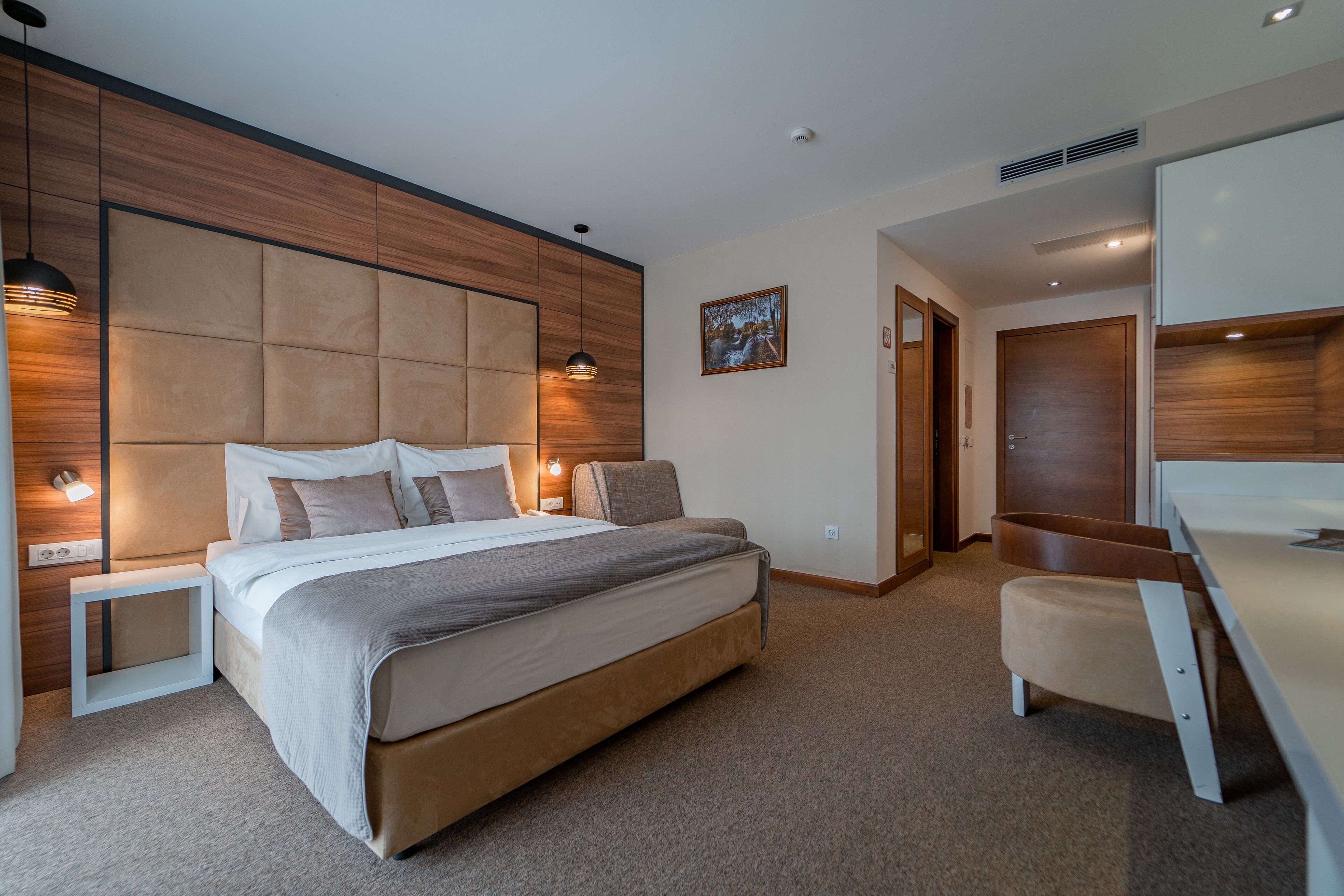 Quarto moderno com uma cama grande, mesas de cabeceira, escrivaninha e guarda-roupa.
