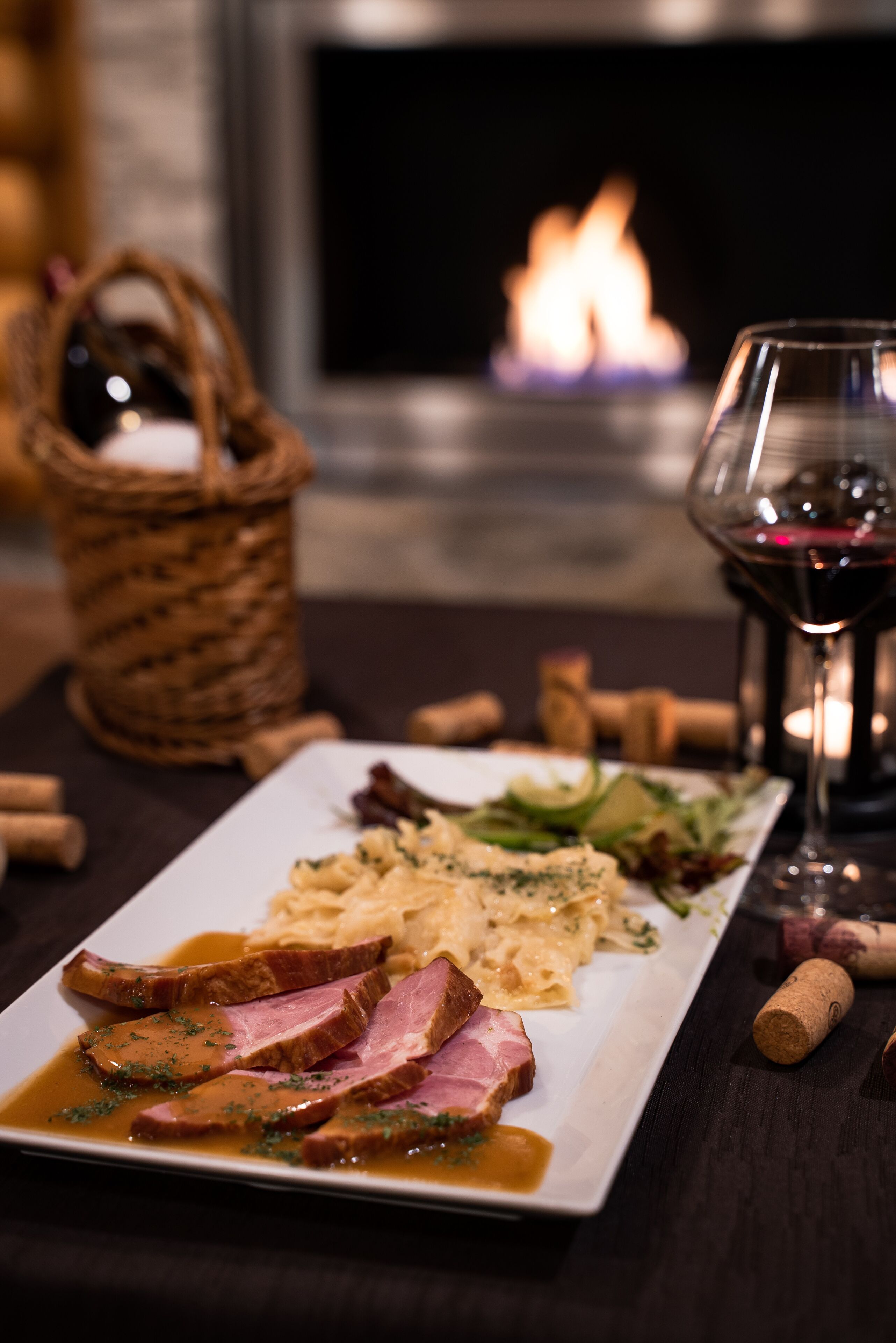 A dining table with a plate of food, a glass of red wine, and a candle.