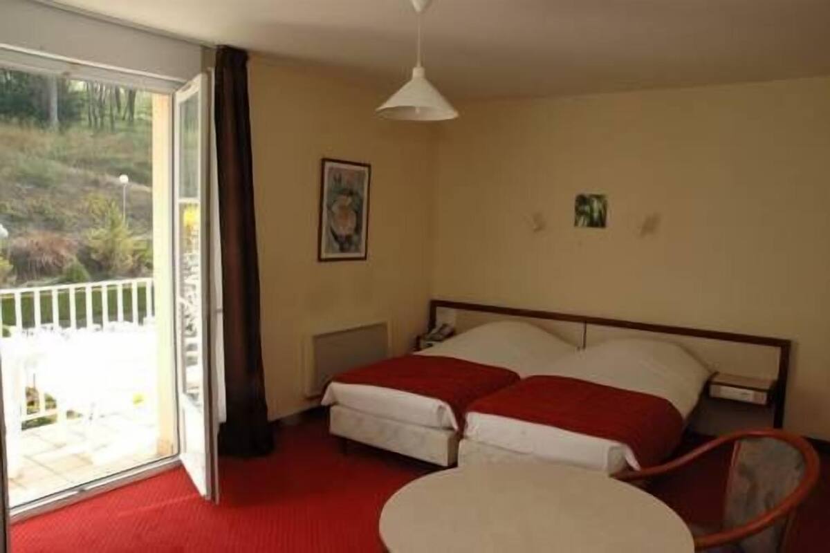 Ein Hotelzimmer mit Bett, Stuhl, Tisch und einem Balkon mit Blick ins Freie.