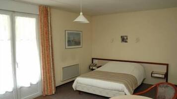 A hotel room with a bed, a bedside table, a chair, a window with curtains, and a ceiling light.