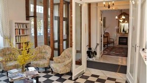 A living room with a checkered floor, a bookshelf, and a door leading to a dining area with a fireplace. - Hotel Restaurant d'Orfeuil (Bourbonne-les-Bains)
