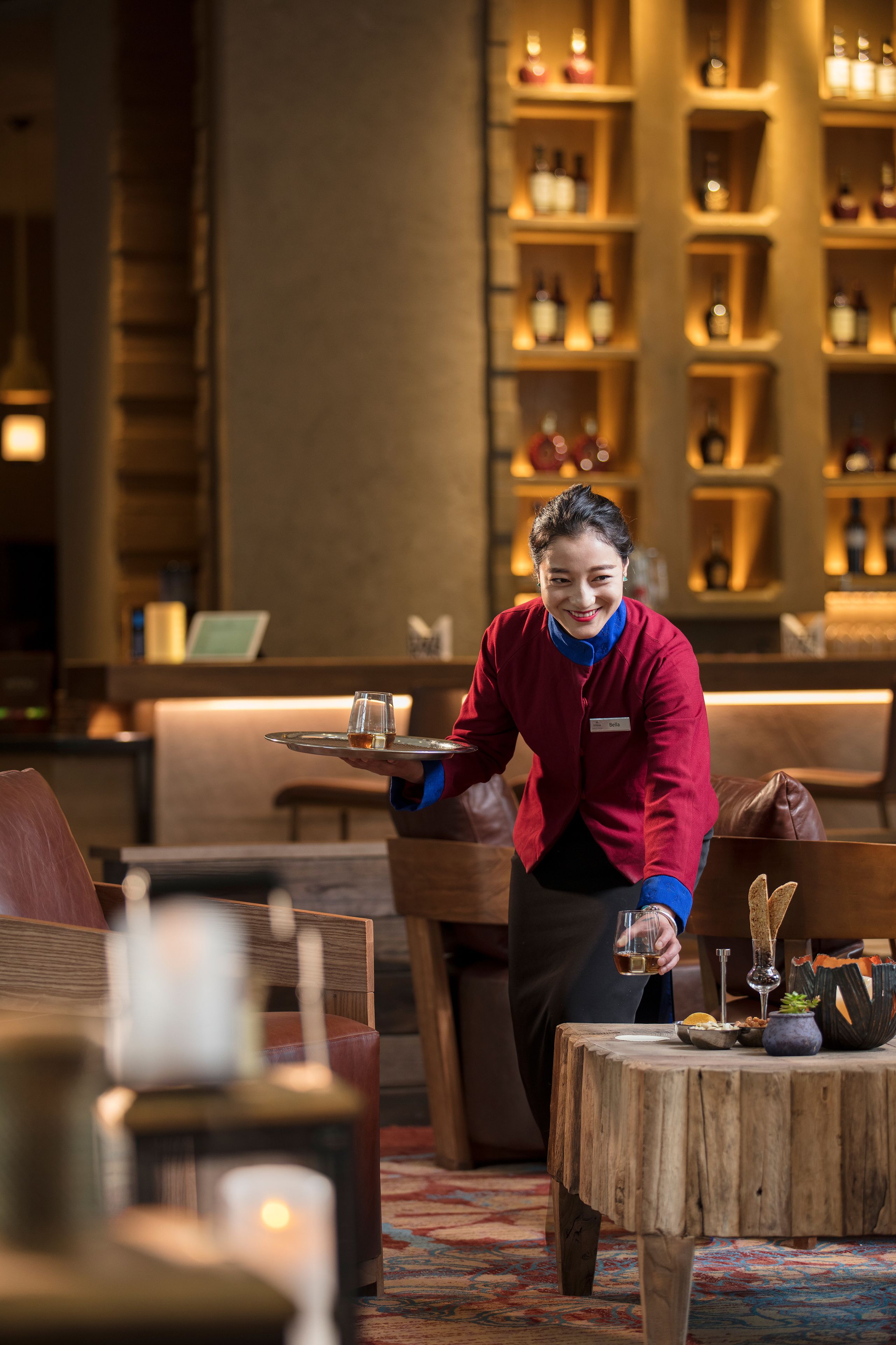 A hotel lobby with a wooden reception desk, a bar area with shelves of bottles, and a cozy seating area with a patterned rug.