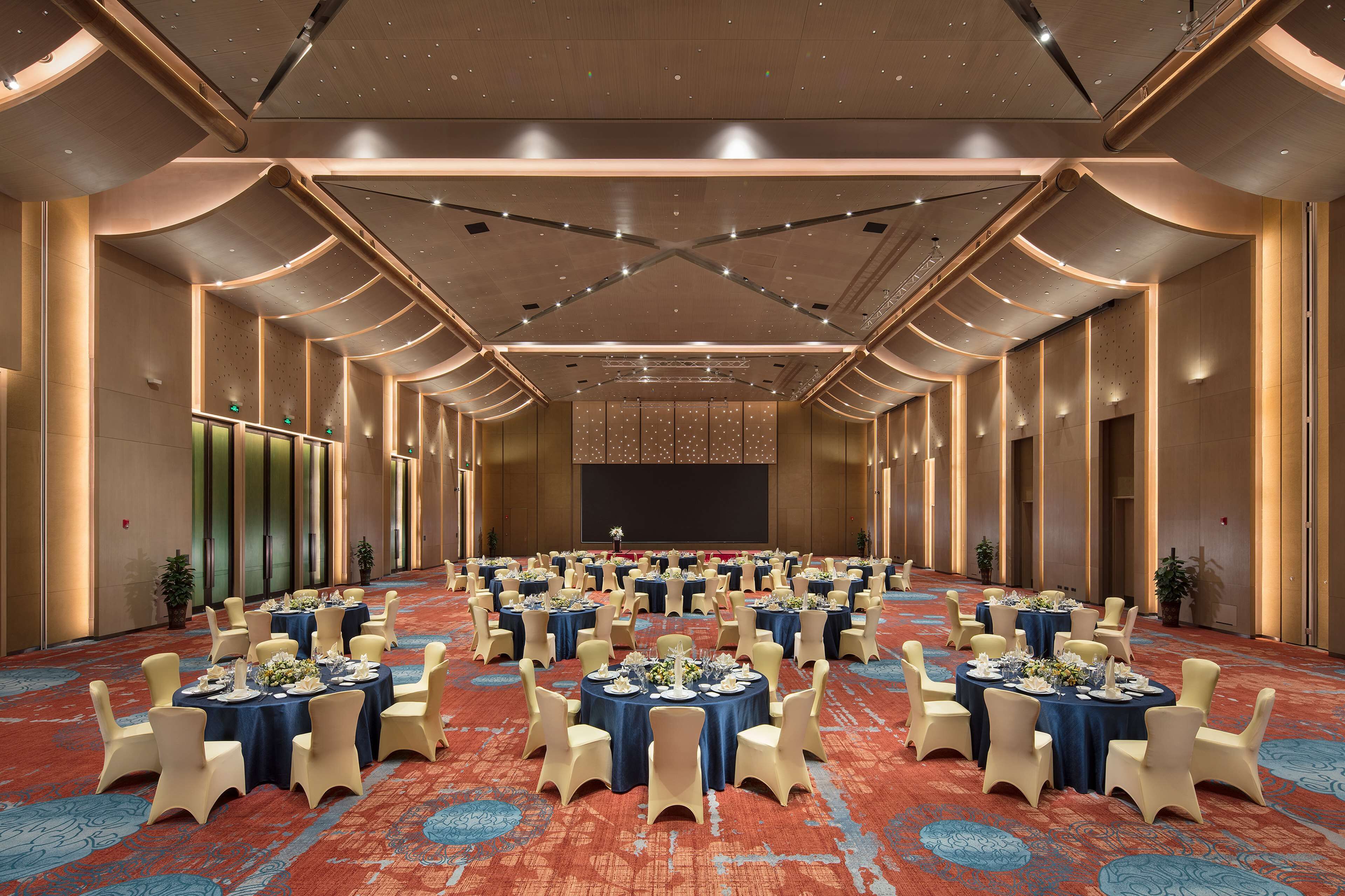 Une grande salle de banquet avec des tables rondes disposées en rangées, prêtes pour le repas.