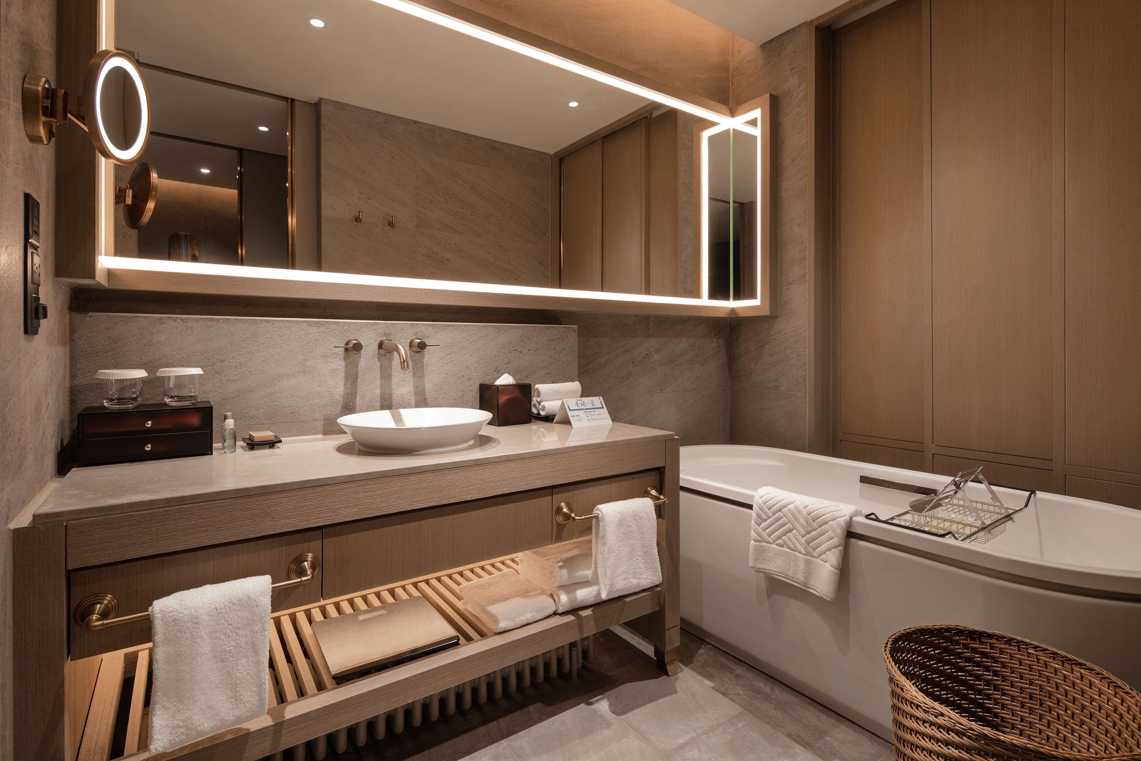 Un baño moderno con un espejo grande, un lavabo, una bañera y un mueble de tocador de madera.