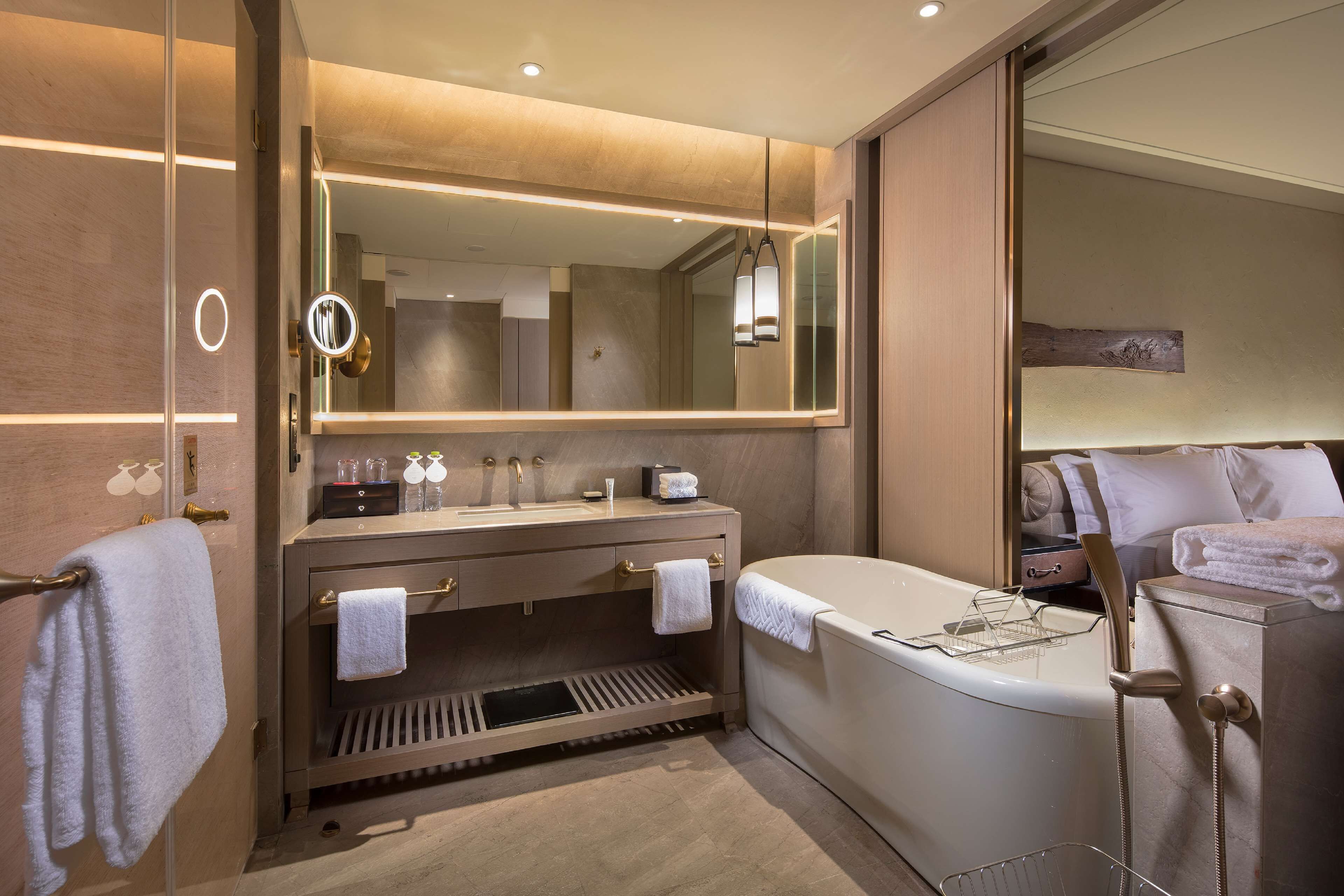 A modern bathroom with a large mirror, a bathtub, and a vanity with a sink and towel rack.