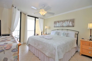 A hotel room with a bed, a nightstand, a table with a tablecloth, a ceiling fan, and a painting on the wall. - Charleston 115 Oceanfront Villas Beach Daze 3 Bedroom Holiday Home By My Ocean Rentals (Folly Beach)