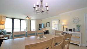Un comedor con mesa y sillas de madera, una araña y vista al salón.