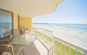 A balcony with a glass table and chairs, overlooking a beach with a pier in the distance. - Charleston 115 Oceanfront Villas Beach Daze 3 Bedroom Holiday Home By My Ocean Rentals (Folly Beach)