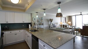 Una cocina moderna con armarios blancos, encimeras de granito e iluminación colgante.