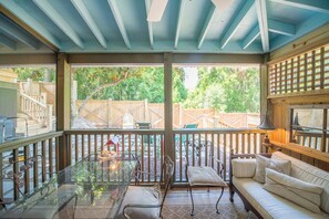 Un patio techado con una mesa de vidrio, asientos acolchados y vista a un jardín trasero.