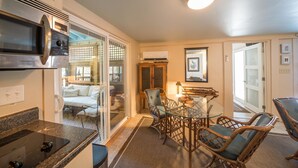 A compact kitchen with a convection oven, a dining area with wicker chairs and a glass table, and a sliding glass door leading to a living area. - Erie The 213 E Hideaway 1 Bedroom Holiday Home By My Ocean Rentals (Folly Beach)