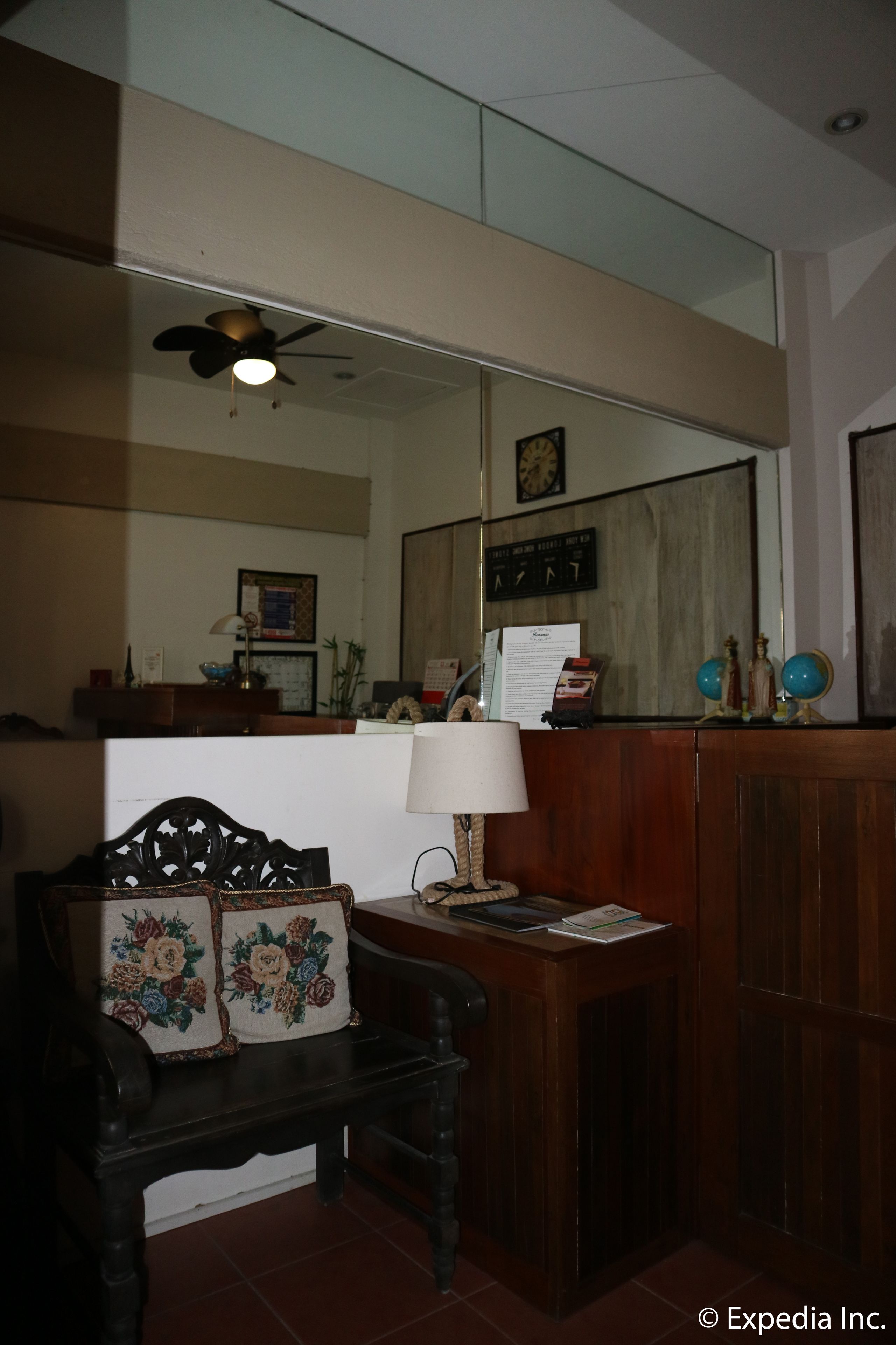 A room with a wooden desk, a chair with floral cushions, a ceiling fan, a mirror, and a clock on the wall.