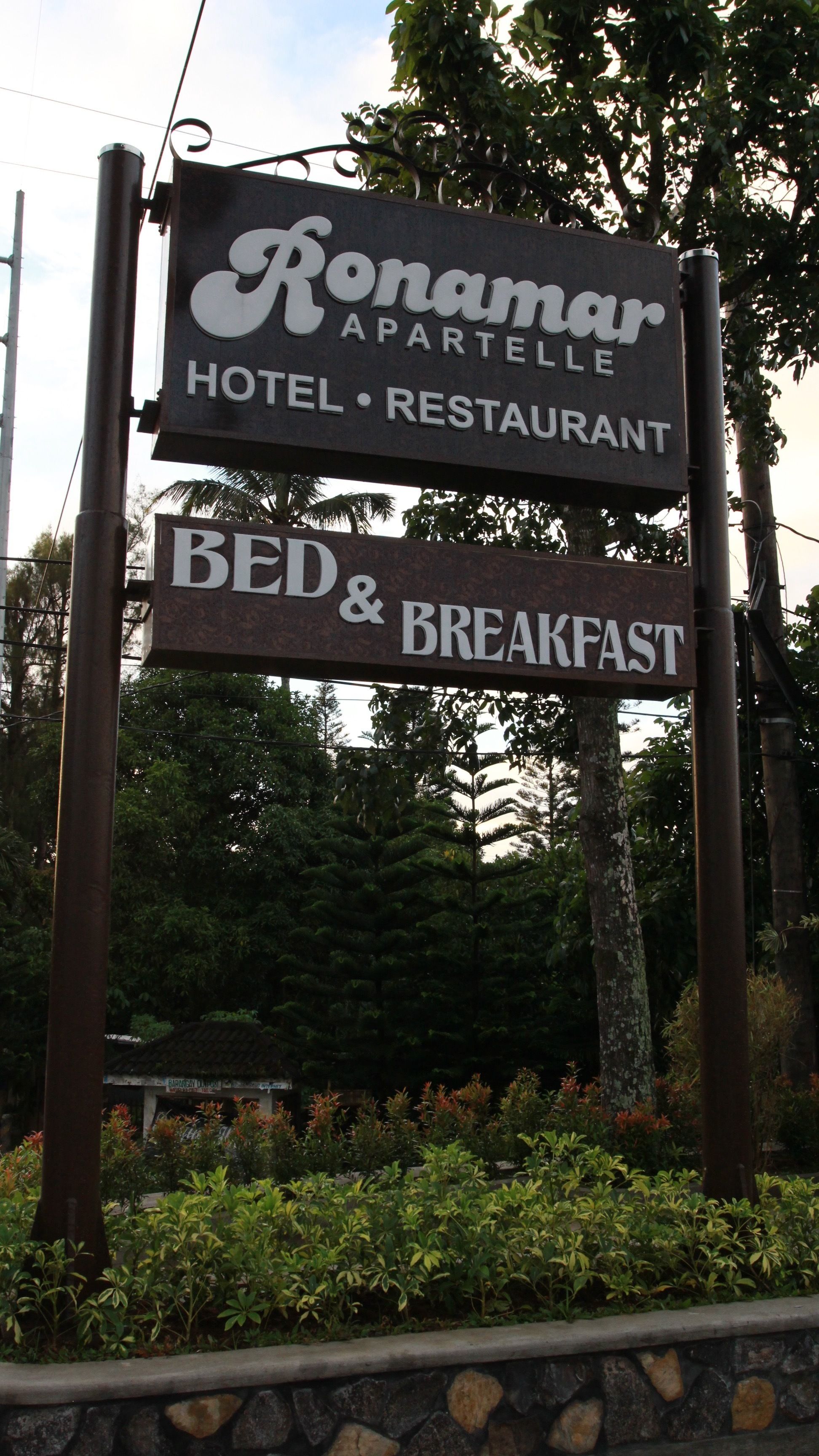 Une enseigne indiquant l’hôtel-restaurant Ronamar Apatelle, et précisant qu’il propose des services d’hébergement et de restauration (formule « chambre et petit-déjeuner »).