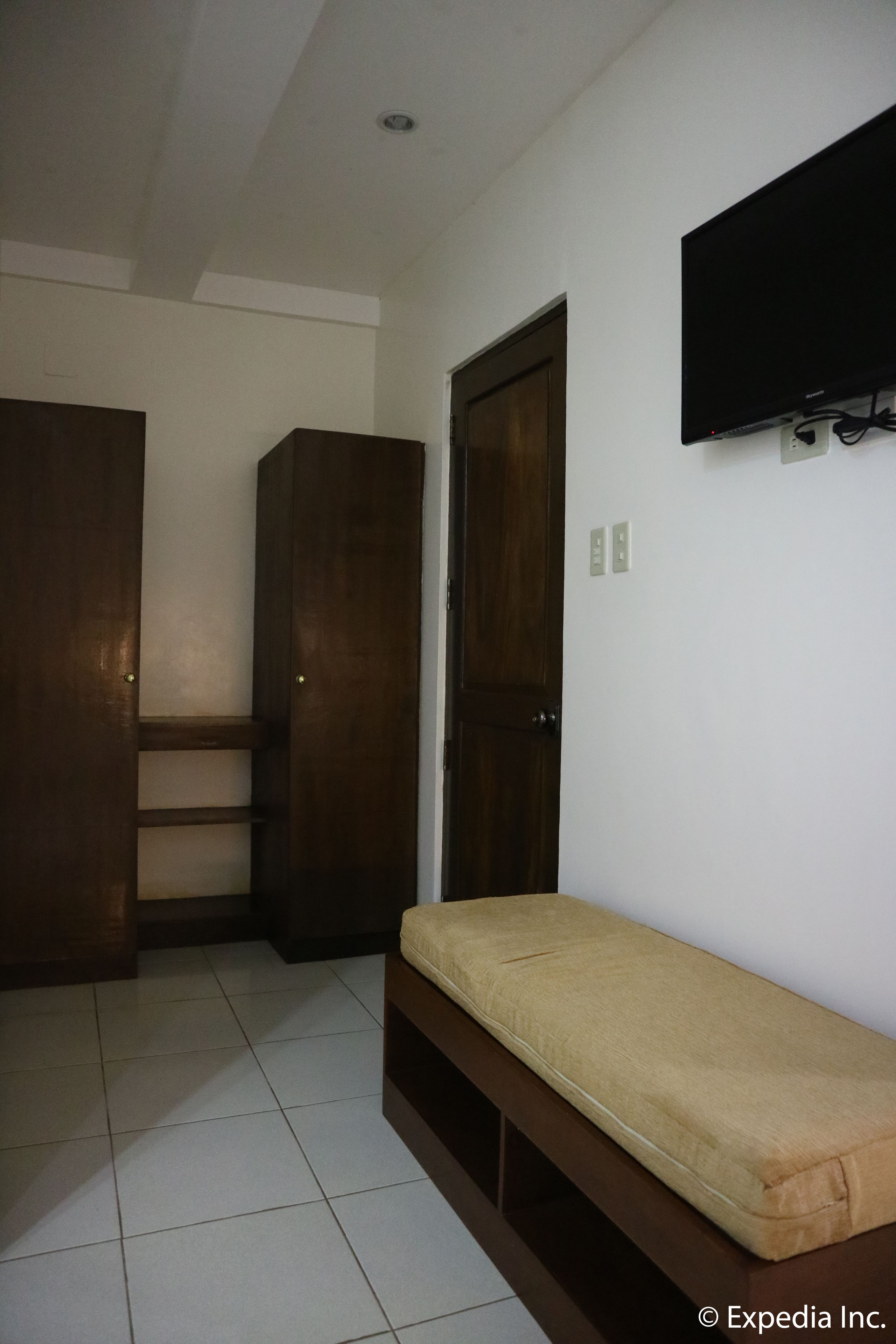 A room with a bed, a wardrobe, a television mounted on the wall, and a door.