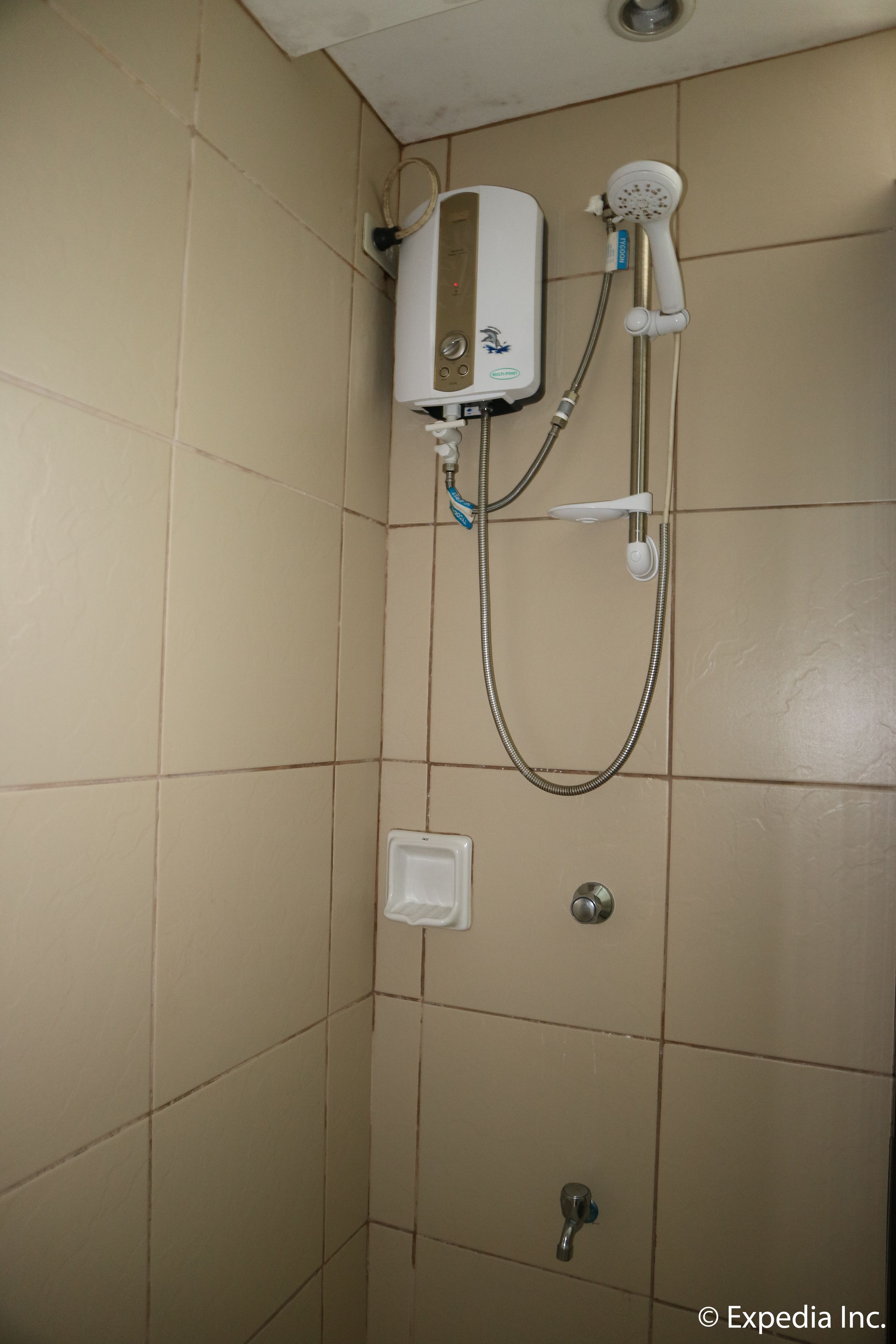 Ein Badezimmer mit beigefarbenen Fliesen, einem weißen Heizkörper, einer Handbrause und einem wandmontierten Wasserhahn.