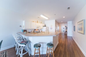 A modern kitchen with white cabinetry, a central island with stools, and a dining area with white chairs.