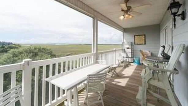 A covered porch with a white railing, a ceiling fan, and a view of a green landscape. - Marsh Winds 2A 3 Bedroom Holiday Home By My Ocean Rentals (Folly Beach)