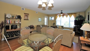 A living room with a glass-top dining table surrounded by wicker chairs, a sofa, and a television. - Turn of the River 2G 3 Bedroom Holiday Home By My Ocean Rentals (Folly Beach)