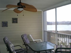 Ein Balkon mit Tisch und Stühlen, einem Deckenventilator und Blick auf ein Gewässer.