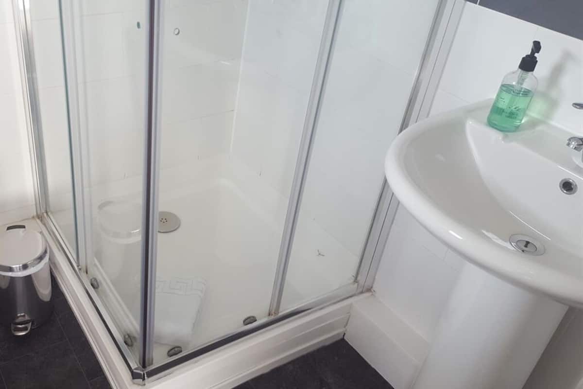Une salle de bain avec une douche à parois de verre, un lavabo blanc et une petite poubelle.
