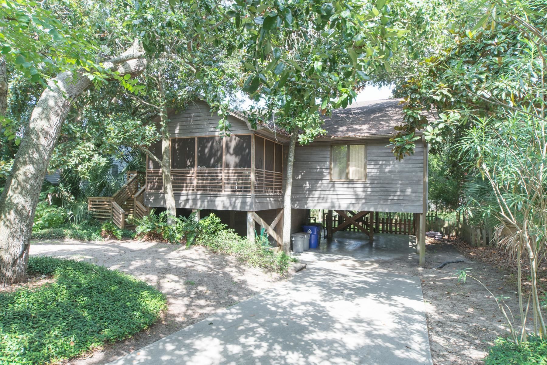 A wooden house with a deck, surrounded by dense foliage and a concrete path.