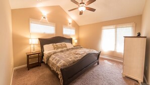 Quarto com cama, duas luminárias de cabeceira, ventoinha no teto e guarda-roupa.