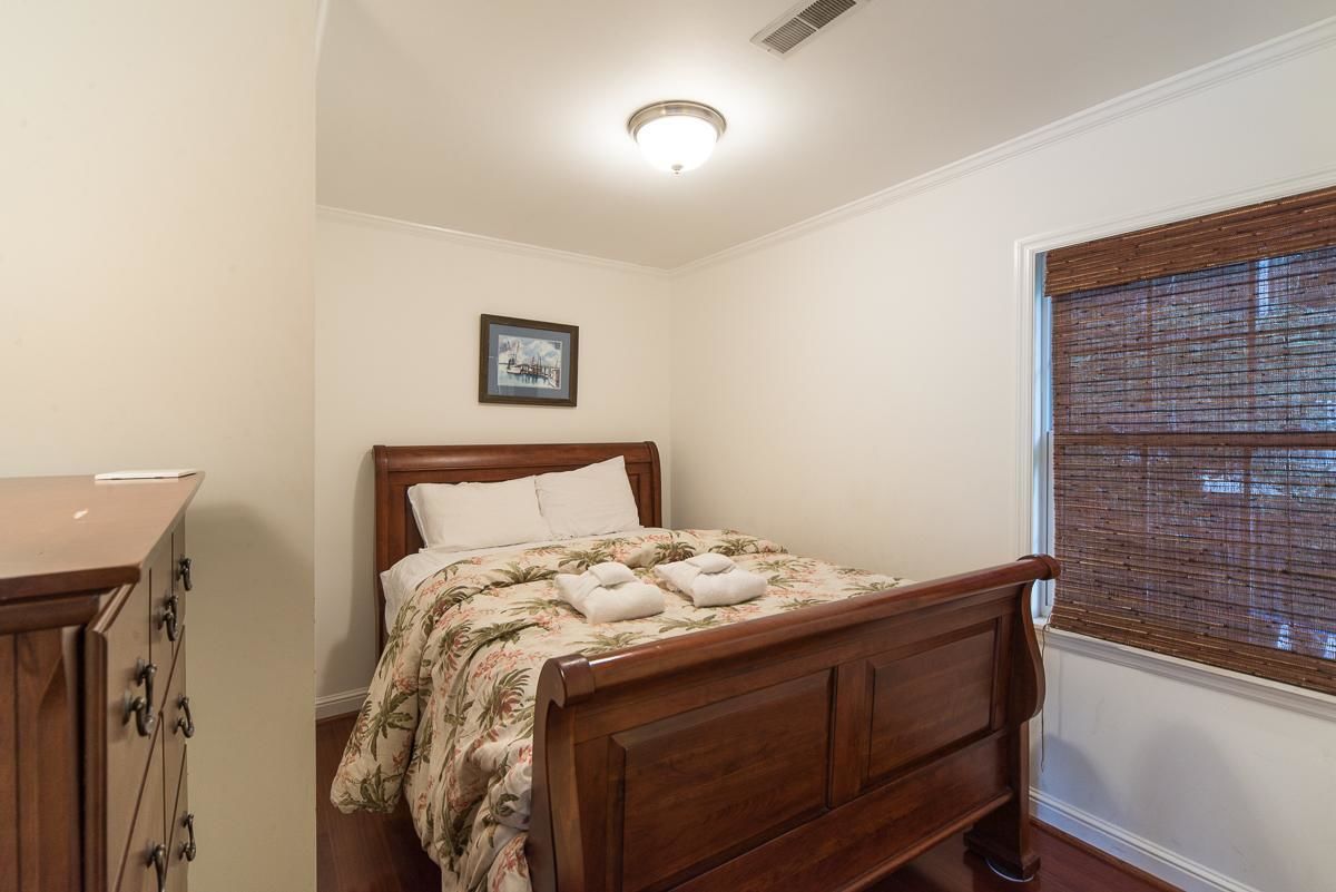 Une chambre à coucher avec un lit en bois, une table de chevet, une commode et une fenêtre avec des stores.