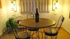 A round dining table with four chairs, a bottle of wine, and two wall-mounted light fixtures.