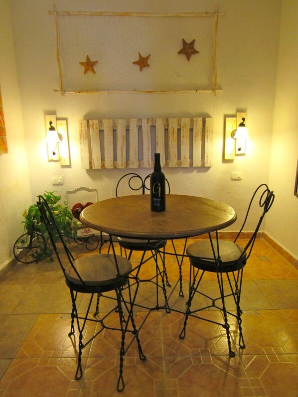 Mesa de jantar redonda com quatro cadeiras, uma garrafa de vinho e duas luminárias fixadas na parede.