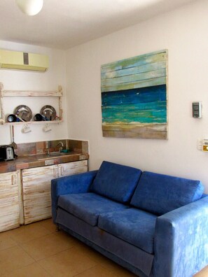 A room with a kitchenette, a blue sofa, and a painting of a beach scene. - Coconut Hotel Boutique (Playa del Carmen)