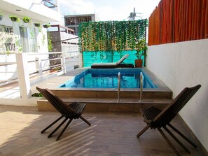 Un área de piscina en la azotea con dos sillones de descanso, un jacuzzi y una pared decorativa con plantas colgantes.