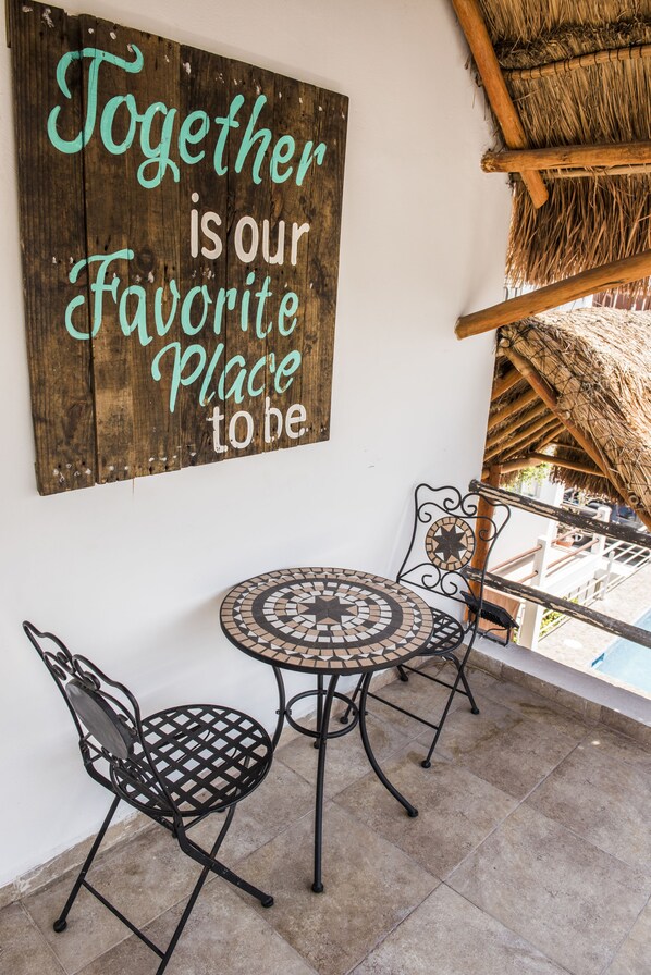 A wooden sign with a message, a round metal table, two chairs, and a thatched roof structure. - Coconut Hotel Boutique (Playa del Carmen)