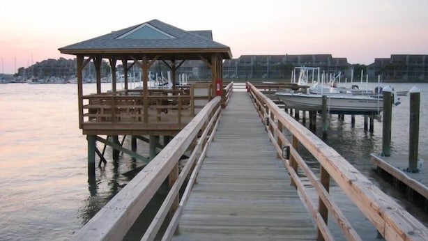 A wooden pier leading to a gazebo with a roof, extending over calm water with boats docked nearby. - Waters Edge Community 95 3 Bedroom Holiday Home By My Ocean Rentals (Folly Beach)