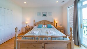 A bedroom with a wooden bed, two bedside tables with lamps, a ceiling fan, and a large window with curtains. - Waters Edge Community 95 3 Bedroom Holiday Home By My Ocean Rentals (Folly Beach)