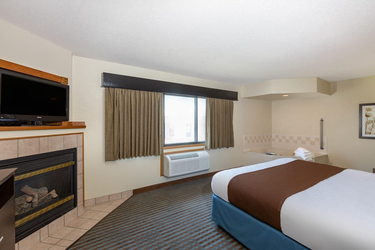 A hotel room with a bed, a television, a fireplace, a window with curtains, and a bathroom.