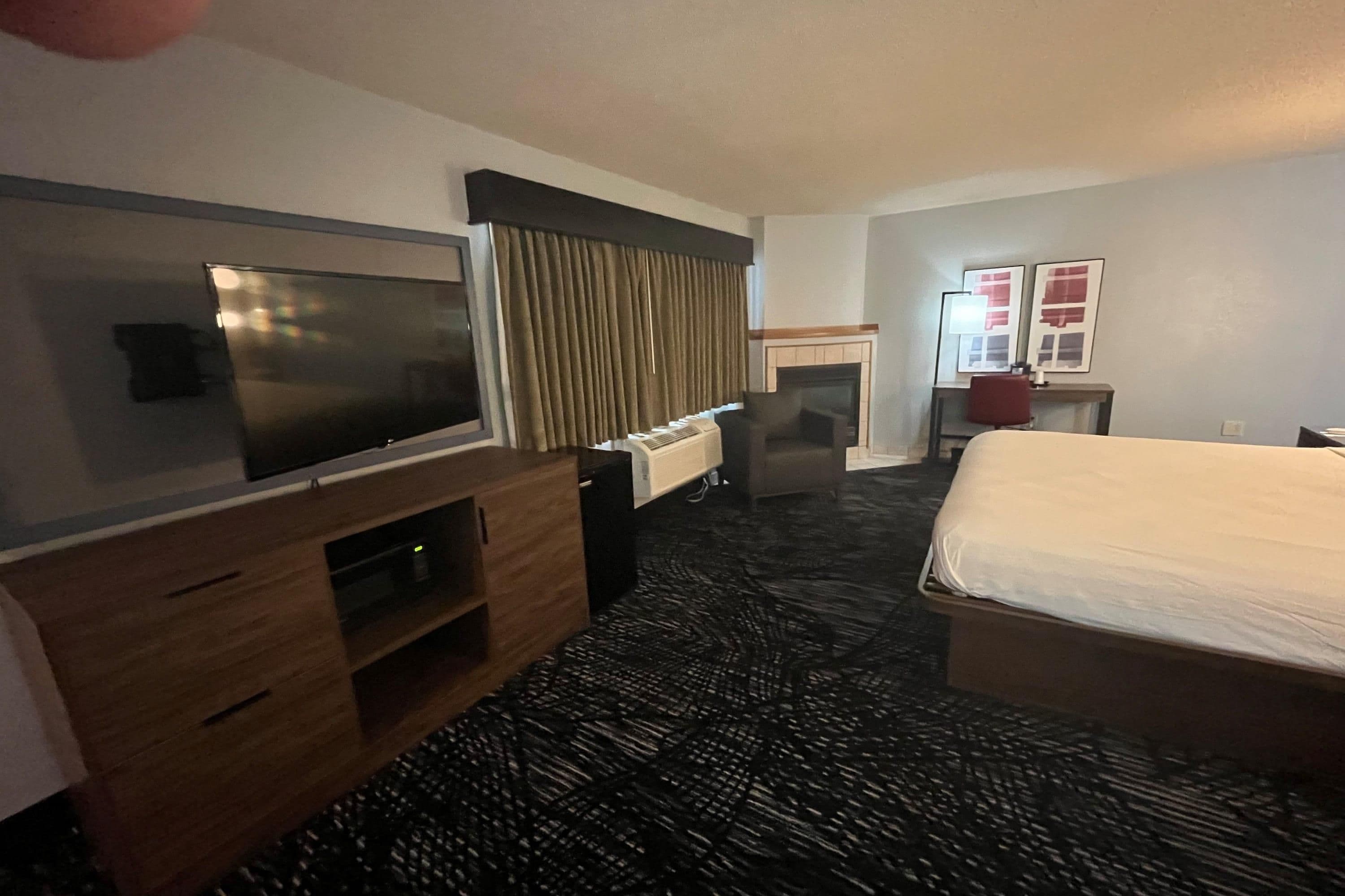 A hotel room with a bed, a television, a desk, and a fireplace.