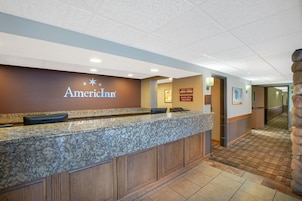 Ein Empfangsschalter mit Marmorplatte, eine braune Wand mit dem Logo des American Inn und ein Check-in/Check-out-Schild.