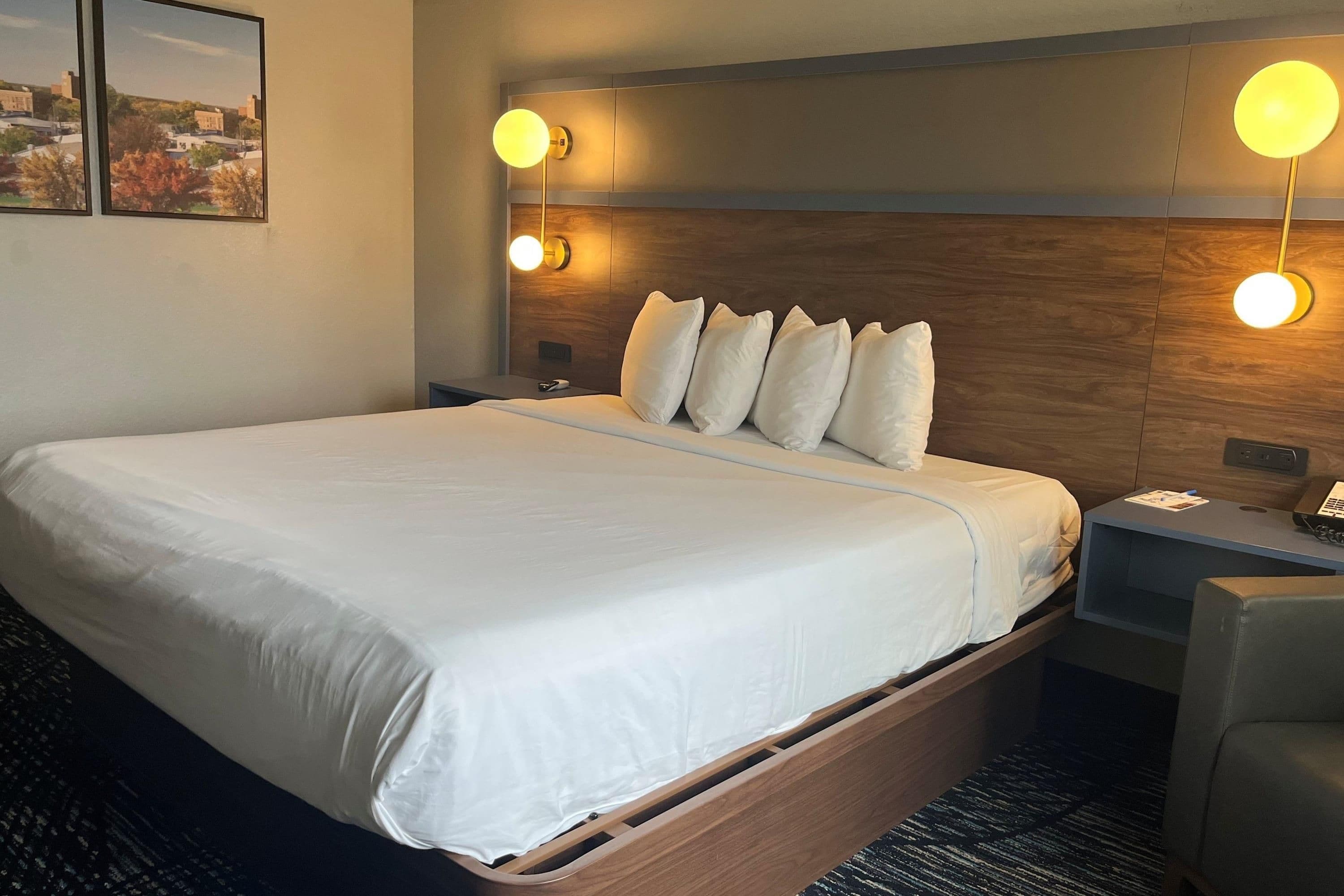 A hotel room with a large bed, a wooden headboard, two bedside tables, a desk, and a chair.