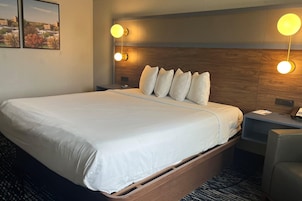 A hotel room with a large bed, a wooden headboard, two bedside tables, a desk, and a chair.