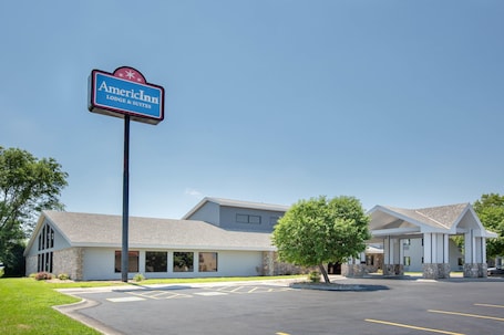 A hotel with a sign reading "AmericInn Lodge & Suites" featuring a modern building with a covered entrance and a parking lot.