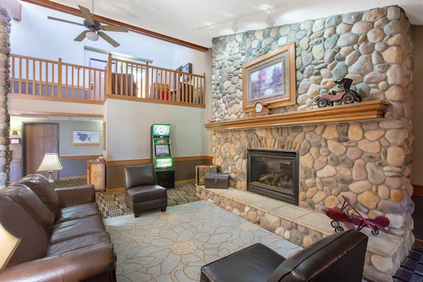 A spacious living area with a stone fireplace, leather sofas, a ceiling fan, and a balcony with wooden railings.