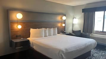 Habitación de hotel con una cama grande, dos mesitas de noche, un escritorio, una silla, una lámpara y una ventana con cortinas.