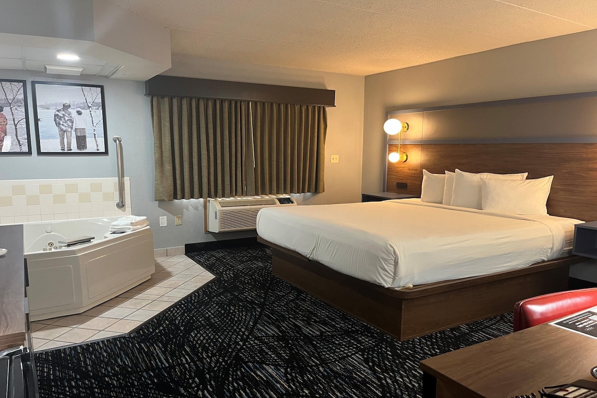 Habitación de hotel con cama, escritorio, silla, baño y televisión montada en la pared.